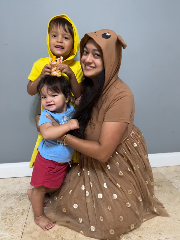 Neem and the kids smiling while Logan waves with his stuffed animal and Rory stands.