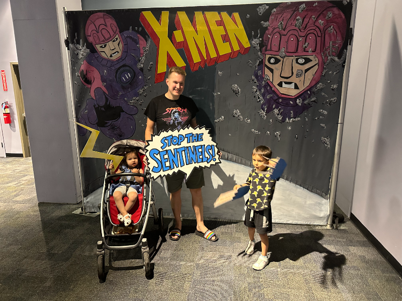 Logan, Ororo, and me standing in front of a X-Men sign dressed up at the Science Center.